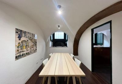 Minimalist meeting room with a light wood table, white chairs, and a historical archway.