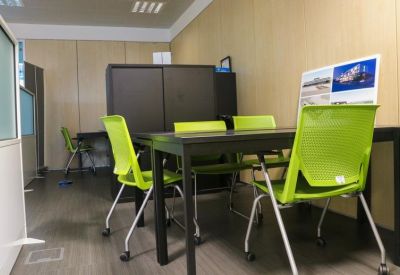 Four-person meeting desk with vibrant green chairs and a wall-mounted poster.