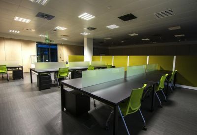 Bright workspace featuring rows of dark desks divided by frosted glass and lime green chairs.