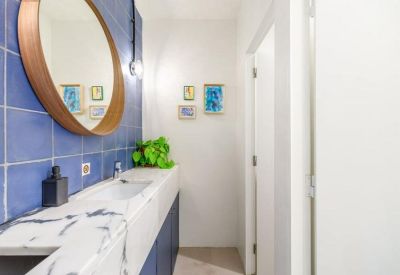 Modern bathroom with blue tiles, marble vanity, and round wooden mirror.