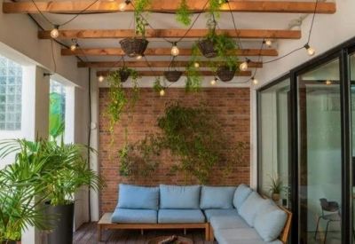 Bright communal lounge with a blue sectional sofa, brick feature wall, and hanging plants under a timber ceiling.