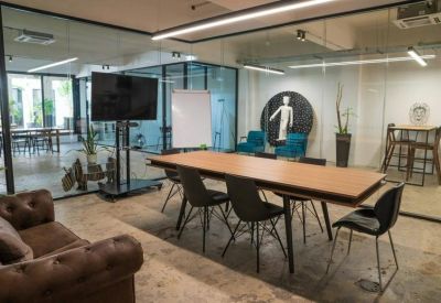 Modern meeting room featuring a long wooden table, black chairs, and a large wall-mounted monitor.