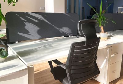 Close-up of a white desk with an ergonomic black chair and privacy screen.