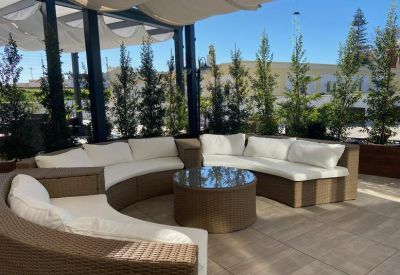 Outdoor terrace lounge with a large curved wicker sofa and glass coffee table.