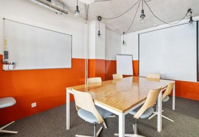 Meeting room with an orange accent wall, wooden table, and whiteboards.