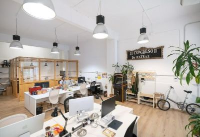 Bright coworking area with white desks, wooden floors, and hanging pendant lights.