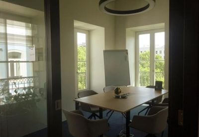 Meeting room with modern grey chairs and a view of trees through tall windows.
