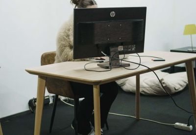 A person working at a wooden desk with a large computer monitor in a quiet office corner.