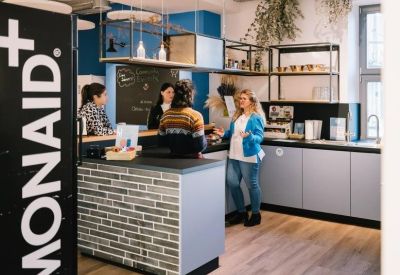 Communal kitchen area with brick-patterned island, wooden floors, and hanging plants.