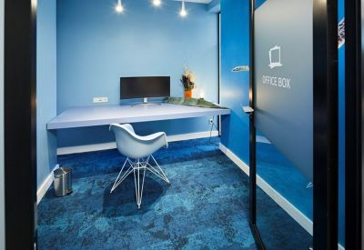 Private office pod with blue walls, patterned carpet, and a large monitor.