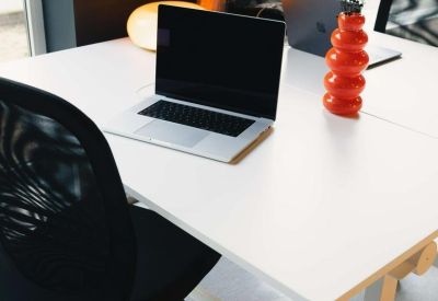 Modern white desk with a laptop and a unique orange bubble vase.