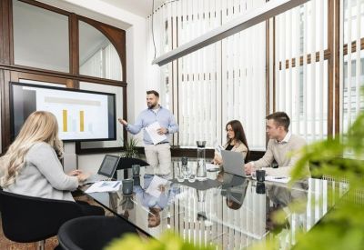 Meeting room with a glass table and a large screen displaying business charts.
