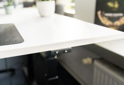 Close-up of a white height-adjustable desk showing the electronic control panel with up and down arrows.