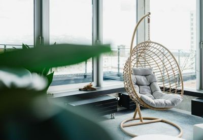 Relaxation area by large windows featuring a modern hanging wicker chair with grey cushions.
