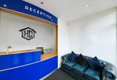 Modern reception area with a blue desk, leather sofa, and branded signage.