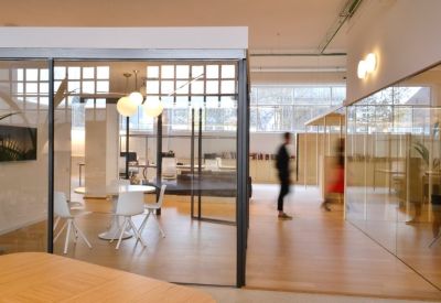Open office area featuring glass partitions, wooden floors, and a white meeting table.