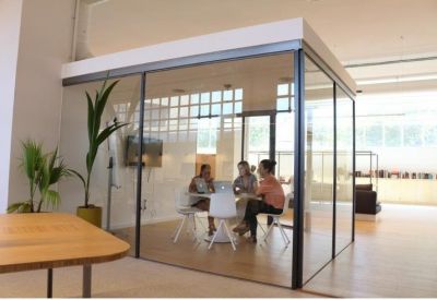 Internal glass-walled meeting pod with people collaborating around a central table.