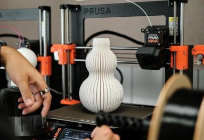 Close-up of a 3D printer creating a white textured vase on a workshop table.