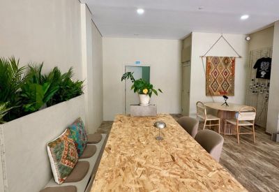 Bright workspace featuring a large OSB desk, built-in bench with colorful cushions, and indoor plants.