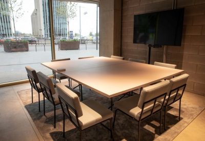 Modern meeting room with a light wood table, grey chairs, and a large wall-mounted monitor.