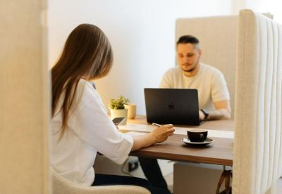 Coworking space with two people working at a wooden table with acoustic privacy screens.