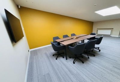 Professional meeting room featuring a long wooden table, dark chairs, and a yellow feature wall.