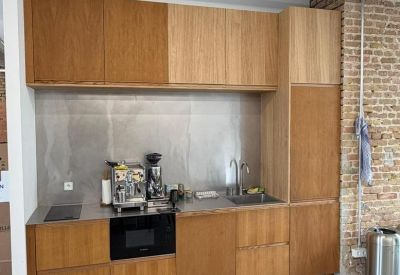 Modern communal kitchen with wooden cabinetry and a professional coffee machine.