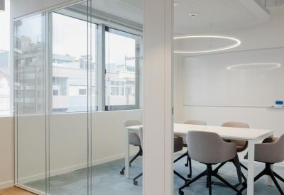Glass-walled meeting room with a white table, grey chairs, and light blue carpet.