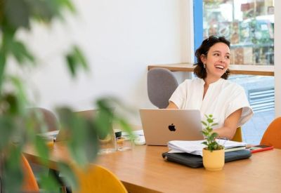 Woman working at a laptop in a bright workspace with natural light.
