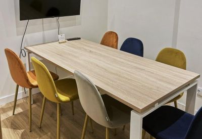 Meeting room with a long wooden table, colorful velvet chairs, and a TV screen.