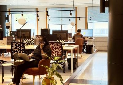 Coworking space with people working at desks, featuring warm lighting and indoor plants.