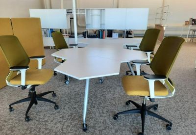 Hexagonal white collaborative workstation surrounded by four mustard yellow ergonomic chairs.