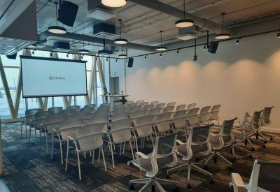 Bright meeting room with rows of mesh chairs, a projector screen, and modern pendant lighting.