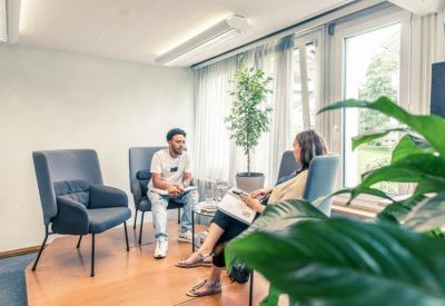 Bright informal meeting area with grey armchairs and wooden flooring.