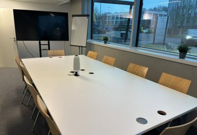 Professional meeting room with a large white conference table and wall-mounted screen.