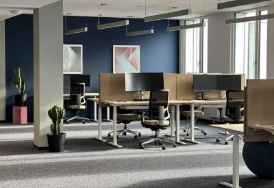 Modern open-plan office featuring several desks, blue accent walls, and natural light.