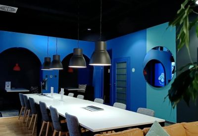 Long white coworking table with blue upholstered chairs and modern pendant lighting.
