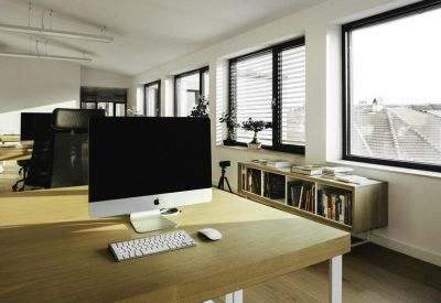 Bright workstation featuring a large monitor on a wooden desk near windows and a bookshelf.