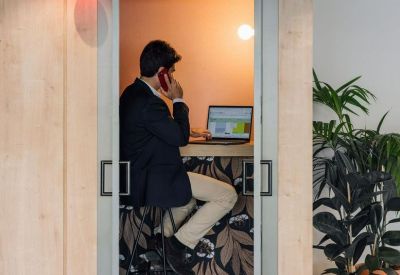 Private glass-enclosed phone booth with a desk and floral wallpaper.