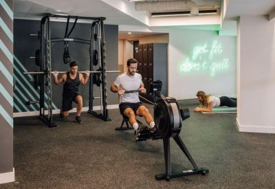 On-site gym featuring a power rack, rowing machine, and neon wall sign.