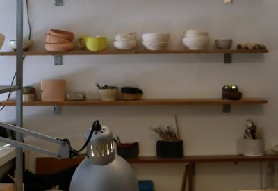 Artistic workspace with wooden wall shelves displaying pottery and an architect's desk lamp.