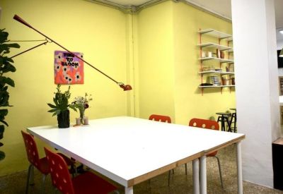 Bright dining or meeting area with a white table, red chairs, and a long-arm wall lamp.