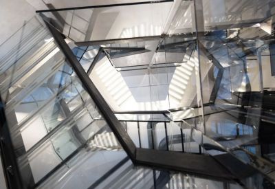 Architectural view of a modern internal glass and steel staircase with geometric light patterns.