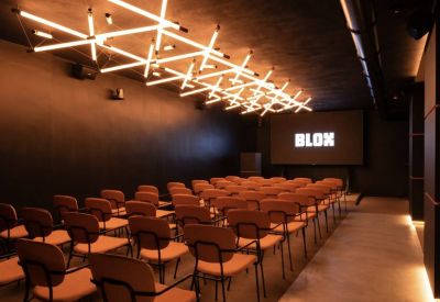 Modern presentation room with rows of orange chairs and a large screen displaying the Blox logo.