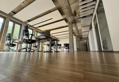 Open-plan workspace with multiple ergonomic desks, chairs, and large windows.