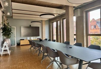 Spacious meeting room featuring a long black table, grey chairs, and a large wall-mounted screen.