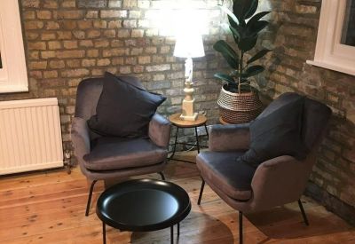 Cozy lounge area with two grey velvet armchairs and a brick feature wall.