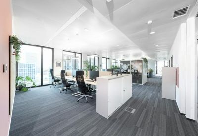 Open-plan office with multiple desks, ergonomic chairs, and large windows.