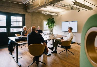 Meeting room with a wooden table, ergonomic chairs, and a wall-mounted presentation screen.