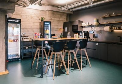 Modern communal kitchen with high stools, a large table, and stocked beverage fridges.